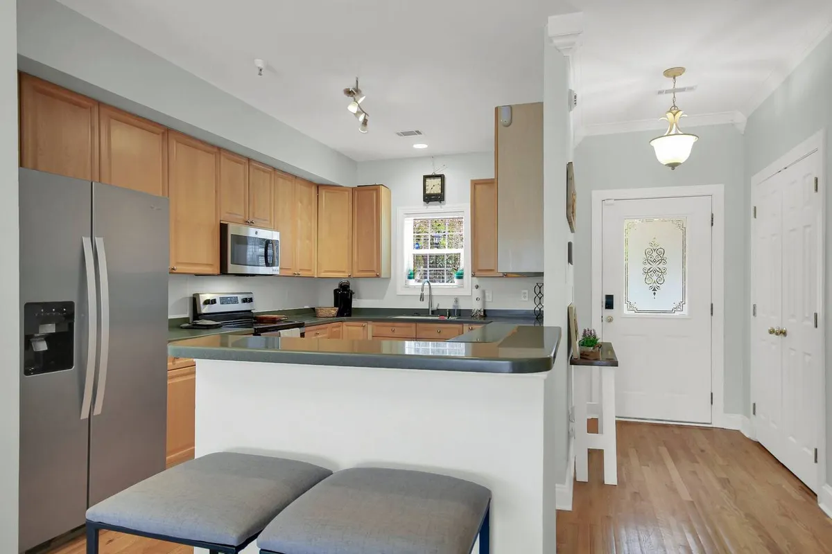 A spacious, modern kitchen with a central island, stainless steel appliances, wooden cabinetry, and an adjoining dining area. The layout allows for easy movement between cooking, dining, and socializing.