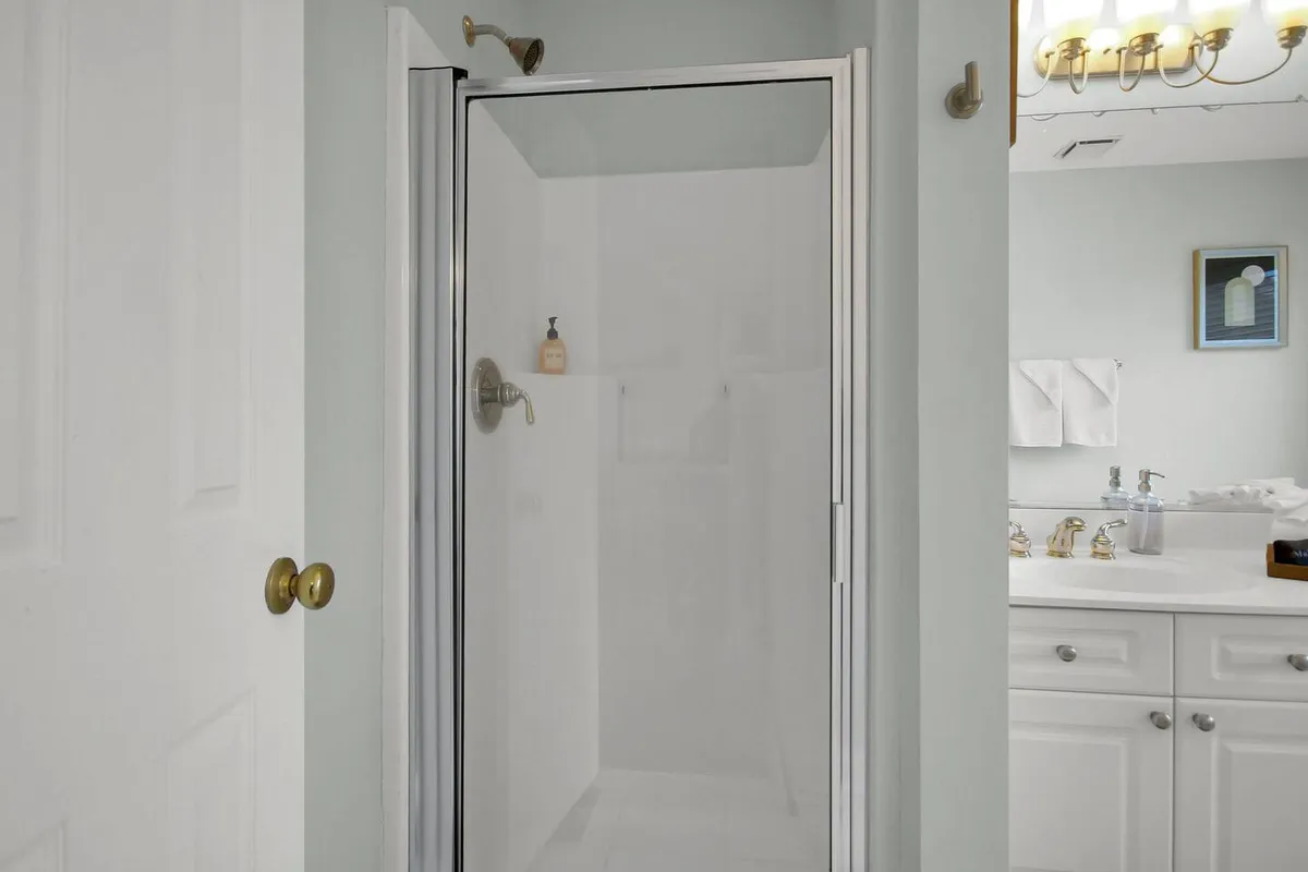 A calming bathroom scene with a glass shower enclosure, white cabinetry, and a decorative light fixture. The space feels fresh and modern, providing a spa-like retreat for relaxation and personal care routines.