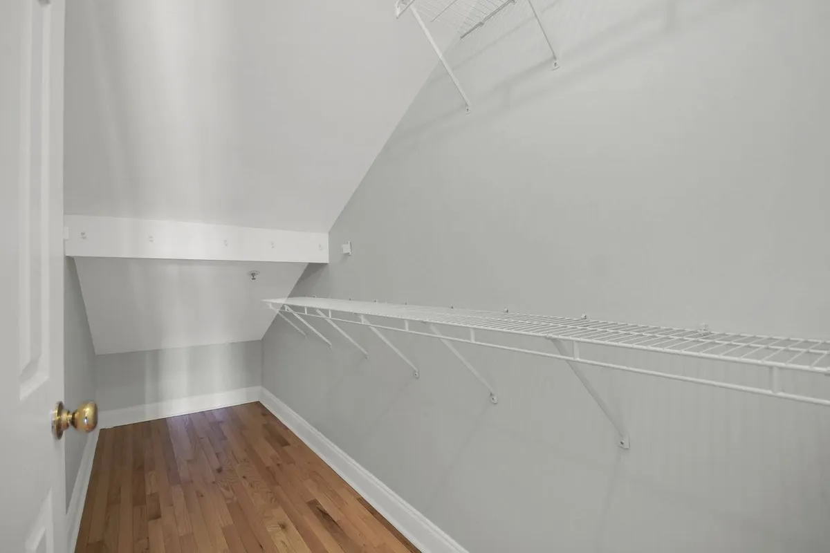 A spacious alcove with shelves, wooden floors, and an angled ceiling, designed for organizing belongings or customizing the area for various purposes. The open, uncluttered space hints at potential uses as a reading nook, play corner, or storage area.