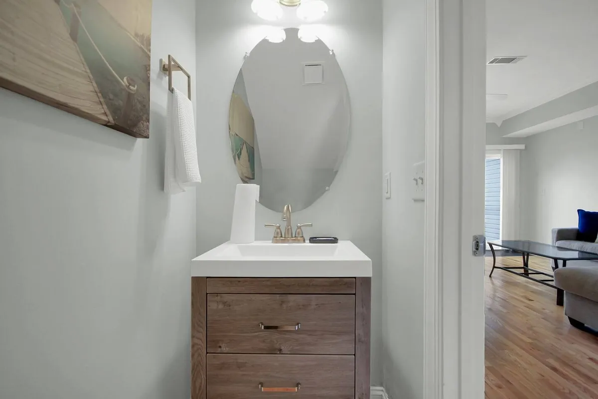 An inviting bathroom with a wooden vanity, sink, and large mirror, set in a warm, functional environment. The space is well-lit and perfect for quick freshen-ups or morning routines.