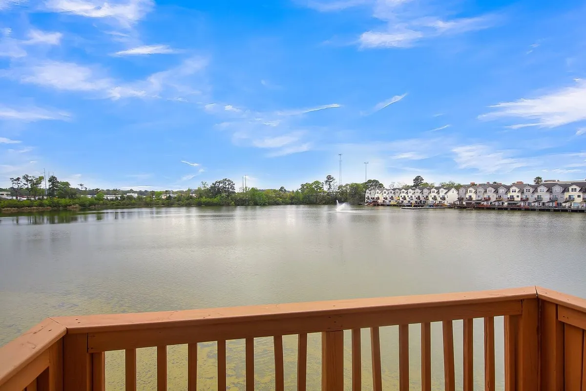 The image captures a calm lake surrounded by greenery, with a fountain and nearby residential buildings. The tranquil water is perfect for activities such as fishing, boating, or simply admiring the sunset. The natural beauty sets the scene for group paddling or tranquil moments outdoors.
