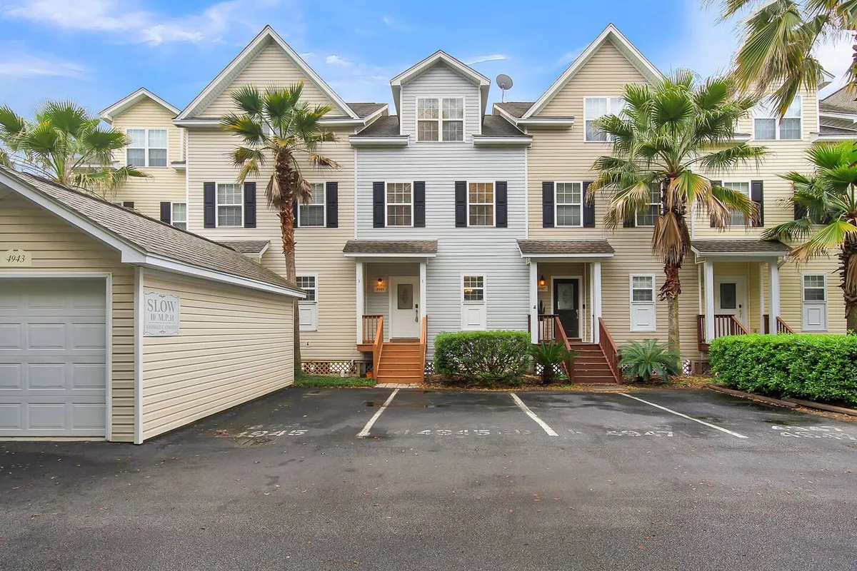 A tranquil exterior view of the townhouse surrounded by stately palm trees, featuring a welcoming driveway and neighborhood signage. The scene captures the charm of the community and the inviting atmosphere for evening walks or morning coffee outside.
