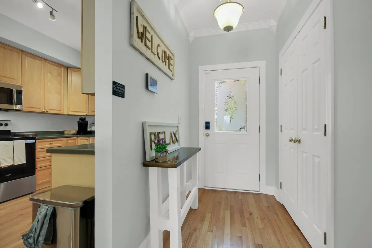 A welcoming entryway featuring a front door, wooden console table, and a decorative 'welcome' sign. The space creates a warm first impression and hints at practical storage possibilities for guests arriving with lake gear.